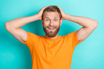 Poster - Portrait of astonished ecstatic overjoyed guy with blond beard wear orange t-shirt hold hands on head isolated on teal color background