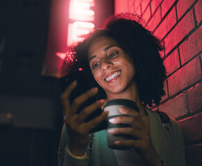 Poster - Happy woman, phone and coffee in city at night by building neon lights, social media and online web location search. Young girl smile, mobile communication and 5g tech streaming on smartphone in town