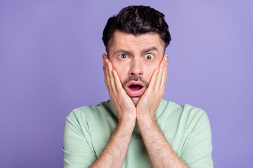 Wall Mural - Photo of scared unhappy handsome guy with brunet hairstyle stubble wear t-shirt palms on cheekbones isolated on purple color background