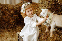  A Cute And Beautiful Little Girl Is Sitting In The Hayloft With A Goat