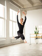 Modern female dancer in black outfit jumping in the air while practices in a dance studio