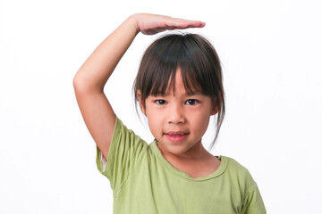 Smiling little girl showing her broken teeth and putting her hand on her head showing growth, isolated on white background.