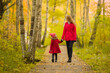 © fotoduets - Happy little daughter and young adult mother walking on trail at birch tree forest. Spending time together in beautiful colorful autumn day. Enjoying stroll. Front view.