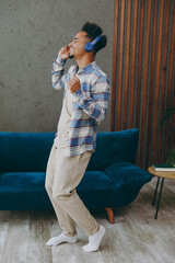 Sticker - Side view full body young man wear shirt headphones dance near blue sofa listen to music stay at home hotel flat rest relax spend free spare time in living room indoor grey wall People lounge concept