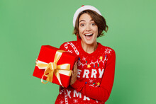Merry Young Woman Wear Knitted Xmas Sweater Santa Hat Posing Hold Red Present Box With Gift Ribbon Bow Isolated On Plain Pastel Light Green Background. Happy New Year 2023 Celebration Holiday Concept.