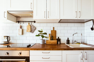 Kitchen brass utensils, chef accessories. Hanging kitchen with white tiles wall and wood tabletop.Green plant on kitchen background 
