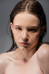 Wall Mural - Portrait of woman with naked shoulders standing behind wet glass on grey background