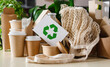 Paper eco-friendly disposable tableware and recycling signs on the background of green plants. The concept of using biodegradable materials.