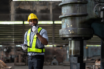 African American male engineer worker checking or maintaining heavy metal machine at the industry factory. Male technician wear safety helmet, uniform working using radio communication in the factory