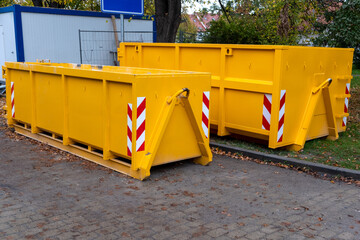 Two yellow metal dumpster containers for construction garbage, house renovation, building of residential apartments. Different size of containers on construction site on the city street, new district.