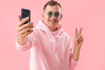 Canvas Print - Young man showing victory gesture while taking selfie on pink background