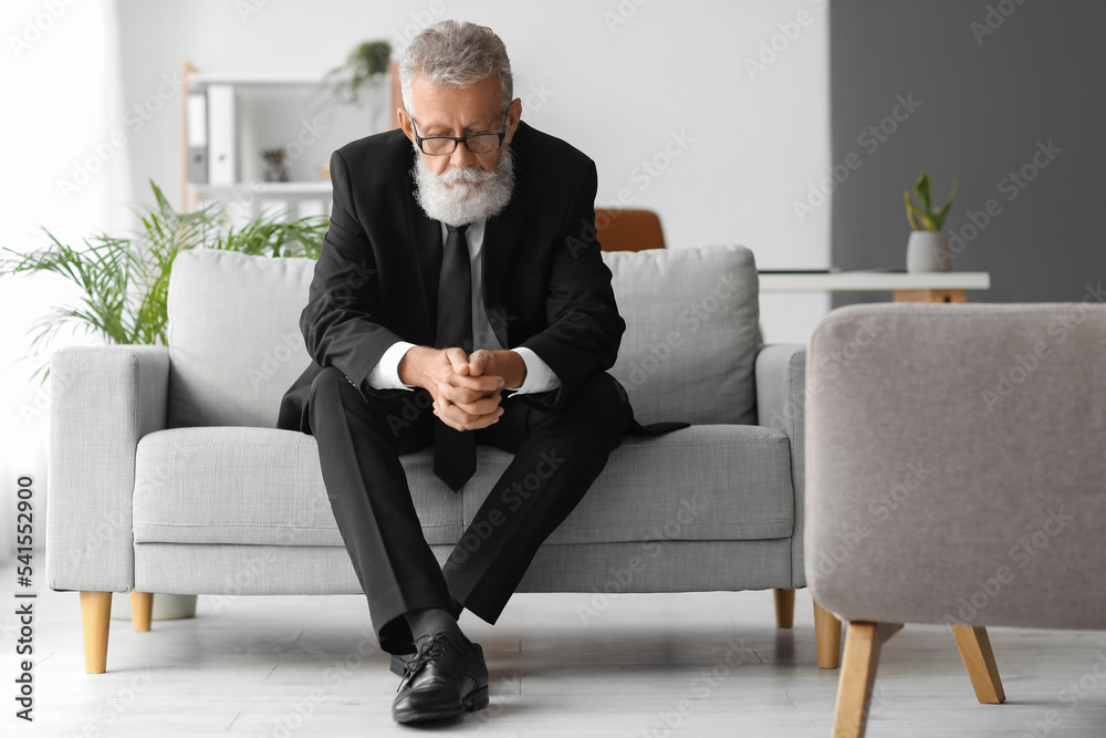 Thoughtful mature man sitting on sofa in office