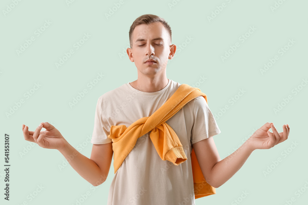Young man meditating on green background
