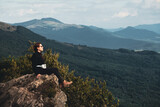 Fototapeta Tęcza - Młoda dziewczyna odpoczywa w górach w czasie wakacji siedząc na skale na szlaku prowadzącym na Połoninę Wetlińską, Bieszczady, Polska