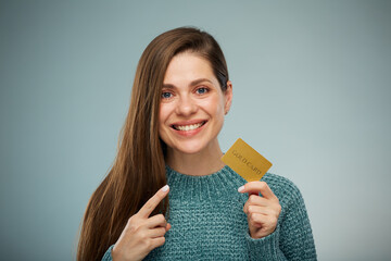 Smiling woman wearing green sweater holding credit card and pointing finger. Advertising female portrait.