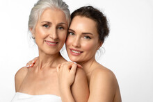 Tender Smiling Daughter Lovingly Hugs Her Elderly Mother By The Shoulders. Beauty Portrait Of Beautiful Women Of Two Generations On White Background.