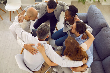 Team of people hugging in office. Group of happy positive smiling diverse international mixed race multiethnic male and female friends sitting in circle holding arms around each other. Support concept