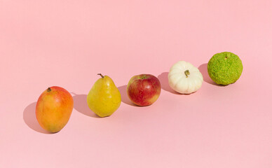 Minimal concept with orange, red, yellow, white and green fruits on sunny day. Creative order on pink background.