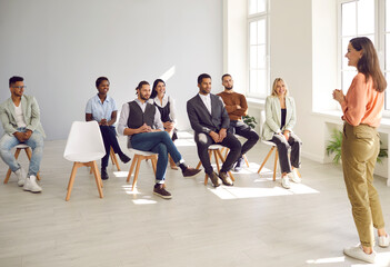 Wall Mural - Smiling young businesswoman stand head lead meeting with multiracial businesspeople in office. Happy female leader or trainer have training or seminar with diverse employees. Education concept.