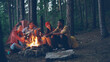 © silverkblack - Male tourist is playing the guitar sitting near campfire with friends singing and having fun, young people are holding sticks with marshmallow above flame. Food, music and fun concept.