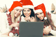 © yurolaitsalbert - three happy young women in costumes of Santa Claus looking at the laptop screen