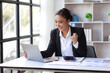 © Wasan - Businesswoman in office looking at laptop screen and showing excitement and joy about a successful business project.