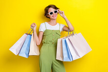 Photo Of Young Cool Celebrity Woman Wear Khaki Stylish Overalls Hold New Sunglass Many Bags Shopaholic Smile Isolated On Yellow Color Background