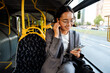 © Drobot Dean - Asian woman in earphones looking at phone screen while traveling in bus