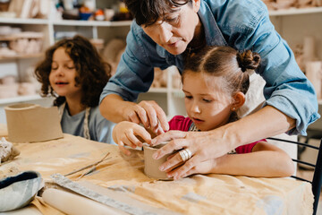 Wall Mural - Mature female teacher sculpting with kids and assisting them at ceramics workshop