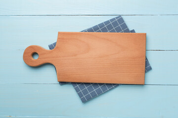 Cutting board with towel on wooden background, top view