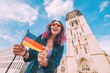 A young happy tourist or student girl with a German flag at the old town or Altstadt in Munster with church belfry in background. Studying language abroad and traveling concept