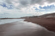 Playa en día nublado con nubes reflejadas en la orilla