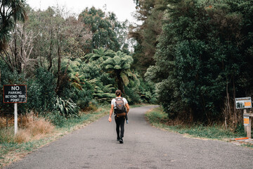 Canvas Print - sporty young man with long hair tied back in a bun walking on nature park entrance road with backpack on his back and tripod on waitawheta tramway, new zealand