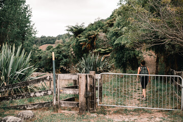 Canvas Print - caucasian girl walking on the path that leads to the forest after crossing the metal fence of a meadow in waitawheta tramway, new zealand