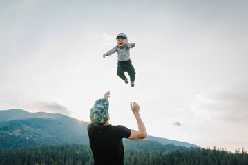 Father throws up his happy son into the sky with his hands. Walking in nature on an autumn day. Dad and baby child playing in the mountains. Concept of family spending time together on vacation.