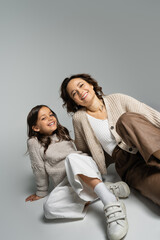 Wall Mural - smiling girl with mother posing in fashionable autumn clothes on grey background