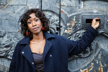 Portrait of a young black model standing against a wooden black door looking at camera