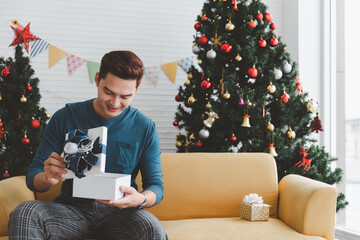 Smiling handsome young man opening white Christmas gift box at home