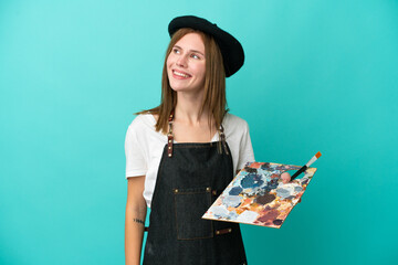 Young artist English woman holding a palette isolated on blue background thinking an idea while looking up