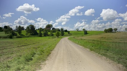 Wall Mural - Green grass in the meadows on a sunny summer day. Latvian landscape with a house on a hill. Blue sky with white clouds over the forest and the road. An old windmill. National Park, Latvia