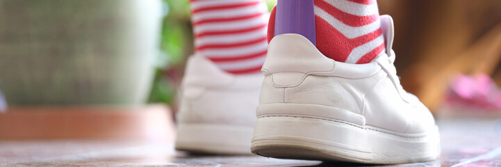 Wall Mural - Man in striped socks putting on white sneakers with shoehorn closeup