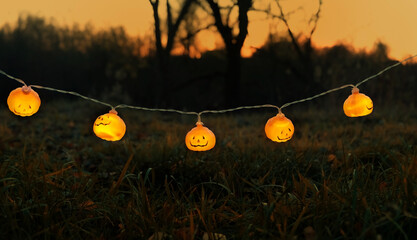 Poster - Orange glowing jack-o' lanterns garland on dark mysterious natural abstract background. symbol of Halloween holiday, Samhain sabbat. autumn season.