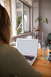 © Austockphoto - Close up shot of back of woman working from home at kitchen table on laptop