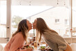© Austockphoto - Female same sex couple kissing across the dining table at home