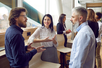 Wall Mural - Different people communicating at a business meeting. Group of men and women standing by an office window, talking, discussing work and sharing opinions on business management. Communication concept