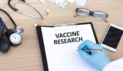 Wall Mural - Paper with text VACCINE RESEARCH writes a doctor's hand sitting at a desk, a medical concept