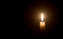 A Single Burning Candle Flame Or Light Glowing On A Spiral White Candle On Black Or Dark Background On Table In Church For Christmas, Funeral Or Memorial Service