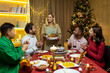 © Liubomir - multiethnic group of happy friends having christmas dinner together at home together. holidays and celebration concept. thanksgiving day The hostess will serve the turkey. reunion party