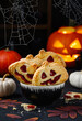 Halloween pumpkin mini pies with  jam. Jack-O-lantern cookies or biscuirs on a black background. Spider web in the frame. Halloween dessert. Selective focus