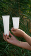 © Маргарита Трушина - cosmetics mockup for design projects. the girl holds a tube for cosmetics in her hand close-up, in the background a green carpet of plants. concept of ecology, natural ingredients, natural cosmetics